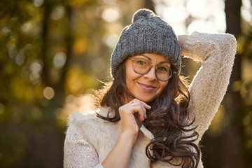 face of a beautiful woman in a cap and glasses on a background of autumn forest