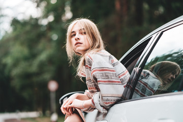 Wall Mural - Pretty hipster woman wearing hanging out of the car window enjoying forest road. Boho style. Wanderlust