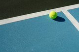 Tennis ball rests on blue tennis court