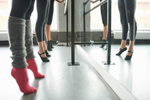 Low Section View At Row Of Elegant Young Women Practicing Ballet Moves Standing By Bar Against Mirror In Dance Studio