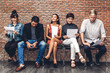 © Art_Photo - Group of business people holding paper while sitting on chair waiting for job interview against brick background