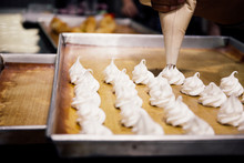 Human Using Pastry Or Piping Bag To Squeeze Out White Whipped Cream Of Meringues On Bakery Tray In Kitchen.