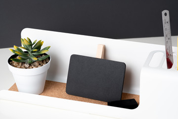 Poster - Black clip blackboard on modern pencil box and green plant in white pot on table and dark grey wall in office desk,mock up space for display of design or text.