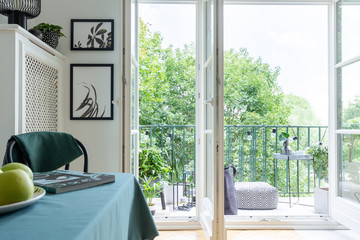 Urban jungle with green plants and trees outside a white dining room interior with place to rest on a beautiful and modern balcony