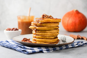 Wall Mural - Stack of pumpkin pancakes with caramel sauce and pecan nuts on a plate, closeup view. Tasty autumn comfort food