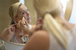 © goodluz - 40-year-old woman putting makeup on in front of mirror