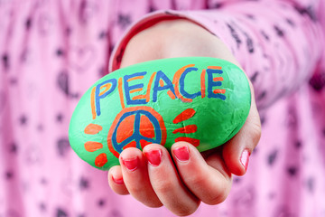 Wall Mural - Child holding painted rock wit PEACE lettering and symbol. Focus on foreground