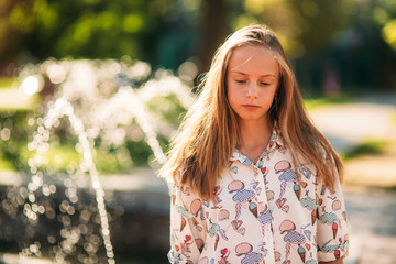 Wall Mural - blond teenage girl in a blond blouse playing with her hair on the background of a fountain