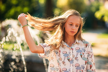 Wall Mural - blond teenage girl in a blond blouse playing with her hair on the background of a fountain