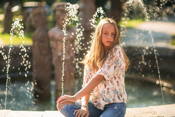 Wall Mural - blond teenage girl in a blond blouse playing with her hair on the background of a fountain