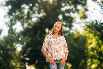 Wall Mural - blonde girl in blouse posing to photographer against the background of green tree