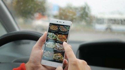 Driver using his smartphone to order pizza online. Man Orders Pizza Using Online Delivery Service With Smartphone. Person sitting in the car and orders using Pizza mobile app