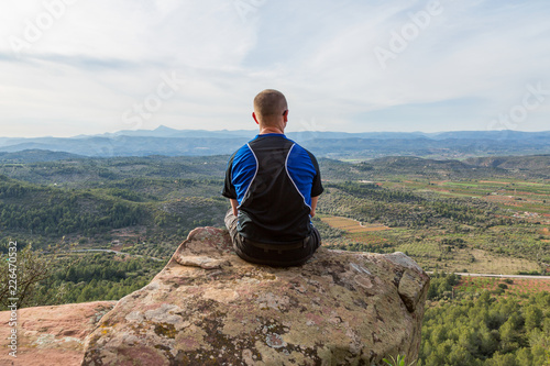Fotografía Man sitter på på bergstopp och tittar på utsikten över dalen