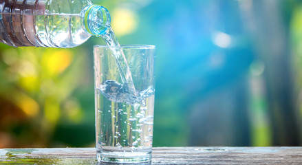 Drink water pouring in to glass over sunlight and natural green background.Water splash in glass Select focus blurred background.