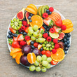 Healthy fruit platter, strawberries raspberries oranges plums apples kiwis grapes blueberries on the dark grey wooden table, top view, copy space for text, square, selective focus