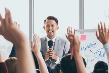 Audience raising hands up while businessman is speaking in training at the office.