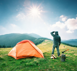 Wall Mural - man on mountain near orange tent looks into the distance