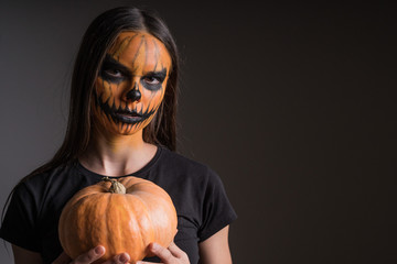 Portrait of a girl in a terrible make-up in honor of Halloween on a black background with a pumpkin