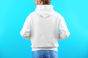 Wall Mural - Man in hoodie sweater on color background. Space for design