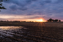 Rural Sunrise Sunset Over A Corn Field After Harvest. Sun Peeks Through Clouds And Makes Colorful Reflections In A Puddle Of Rain Water With Room For Copy 