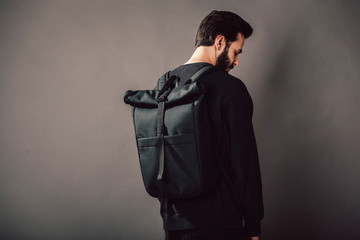 Wall Mural - Stylish young guy wearing black blank  and backpack, horizontal studio portrait