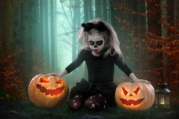 Little girl in a costume of witch posing with pumpkins over fairy background. halloween