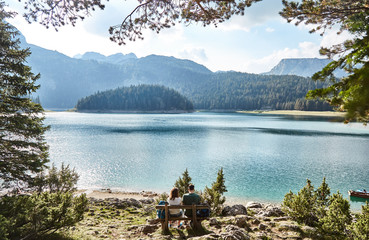 Wall Mural - a young couple sitting on a bench. black lake. durmitor national park. montenegro.