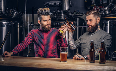 Two stylish bearded hipsters friends drinking beer together at indie brewery.