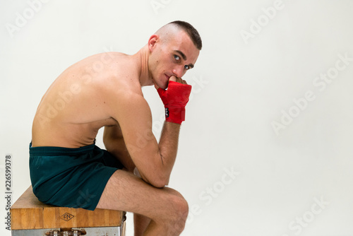 Fotografie, Obraz pugile a torso nudo con fasce da boxe e shorts neri su sgabello di legno