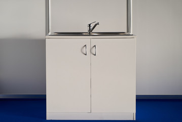 White cabinet kitchen sink with chrome water tap against white wall background. 