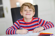 © Irina Schmidt - Happy smiling little kid boy at home making homework at the morning before the school starts. Little child doing excercise, indoors. Elementary school and education: Boy writing letters and numbers.