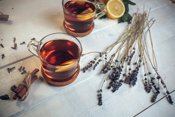 Two full Cups of black tea with lemon, with lavender, dry cloves, fresh mint and cinnamon sticks, on a white wooden table, still life