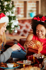 Wall Mural - Friends giving gifts to each other while sitting at table. In background Christmas tree. Christmas holidays concept.