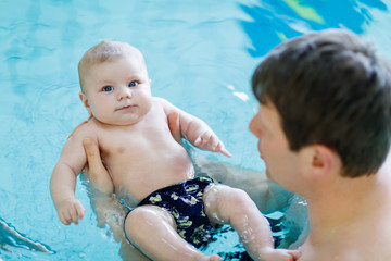 Wall Mural - Happy middle-aged father swimming with cute adorable baby in swimming pool.