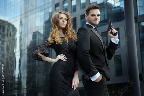 Photographie  An elegant man with pistols in his hands protects a beautiful girl