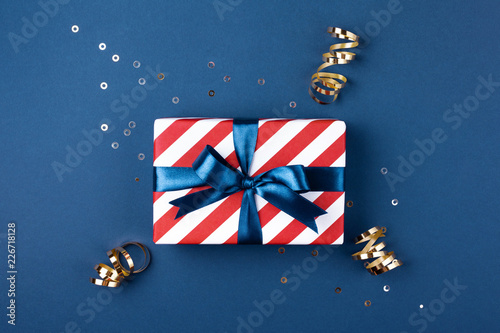 Gift box wrapped in red striped paper and tied with blue bow on blue backgrou...