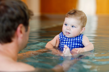 Wall Mural - Happy middle-aged father swimming with cute adorable baby girl in swimming pool.