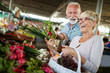 © NDABCREATIVITY - Smiling senior couple holding basket with vegetables at the market