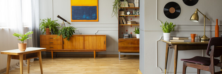 Chair at desk with gold lamp in grey apartment interior with plants on wooden cabinet. Real photo