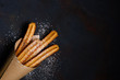 Churros sticks fresh hot in paper bag on dark background with copy space