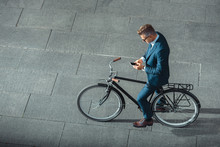 high angle view of businessman in formal wear using smartphone while standing with bicycle on street