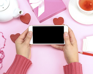 two female hands in a pink sweater holding a white smartphone