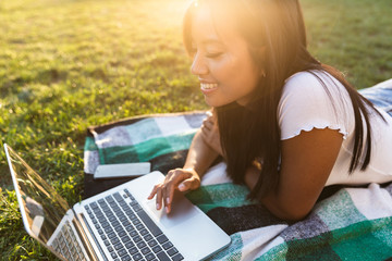 Poster - Smiling young asian girl outdoors in park using laptop computer.