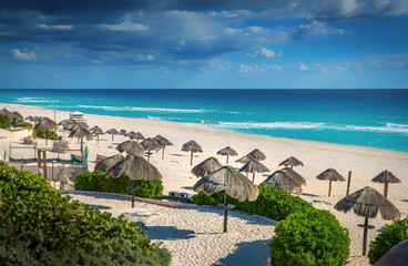 Wall Mural - Cancun beach in mexico with umbrellas in the sand, beautiful blue water with dramatic clouds