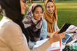 © Drobot Dean - Arabian women students using mobile phone in park outdoors.