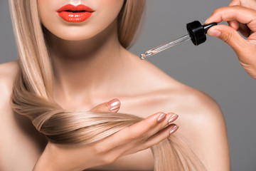 cropped shot of beautician applying lotion on hair of beautiful girl isolated on grey