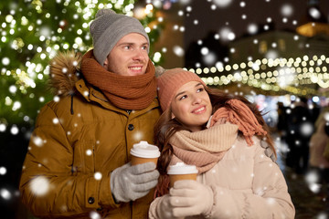 Sticker - winter holidays, hot drinks and people concept - happy young couple with coffee at christmas market in evening