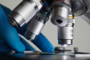 Wall Mural - scientist hands with sample slide on microscope close-up shot in the laboratory