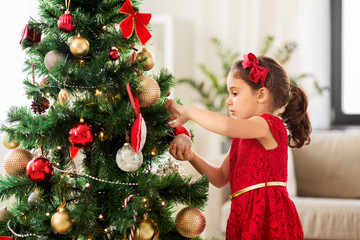 Wall Mural - winter holidays and people concept - happy little girl decorating christmas tree at home