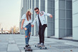 Happy young couple having fun while driving skateboards on a modern street.